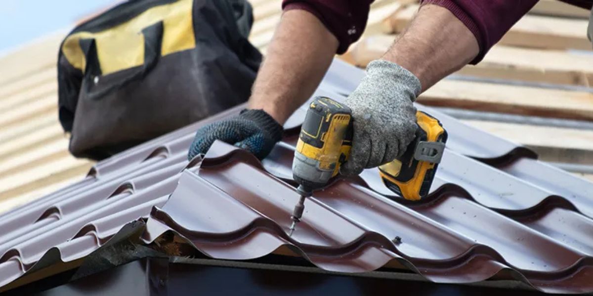 A man drills to install a metal roof, emphasizing the importance of regular roof maintenance to prevent leaks.