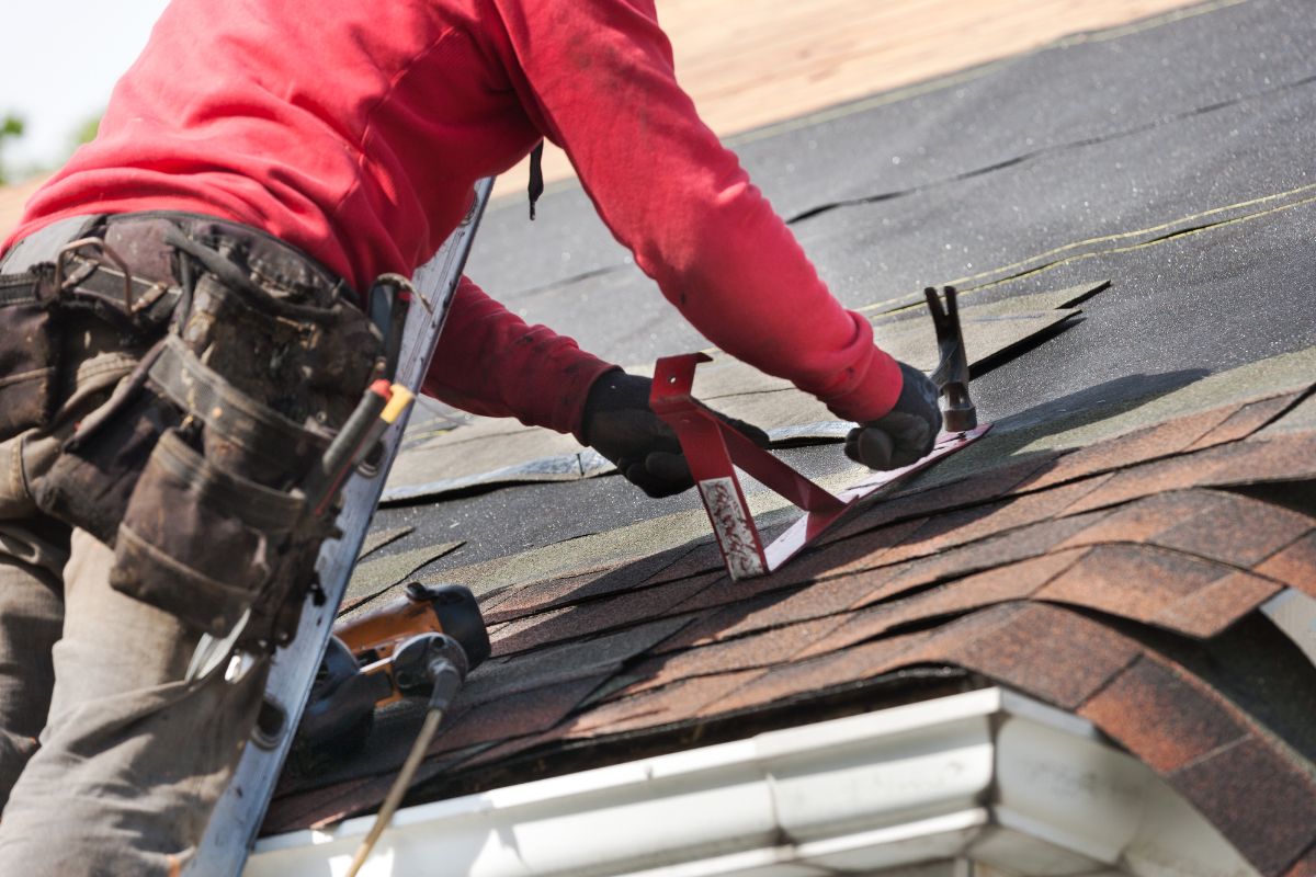 A man using a tool while working on a roof, focused on his task under clear blue skies.